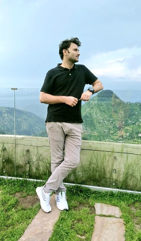 Ahmed Qureshi standing outdoors in front of green hills.